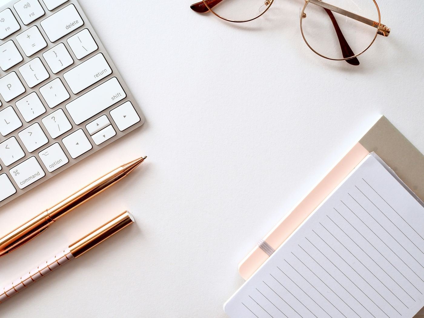 Desk with a keyboard, notepad, pens and reading glasses